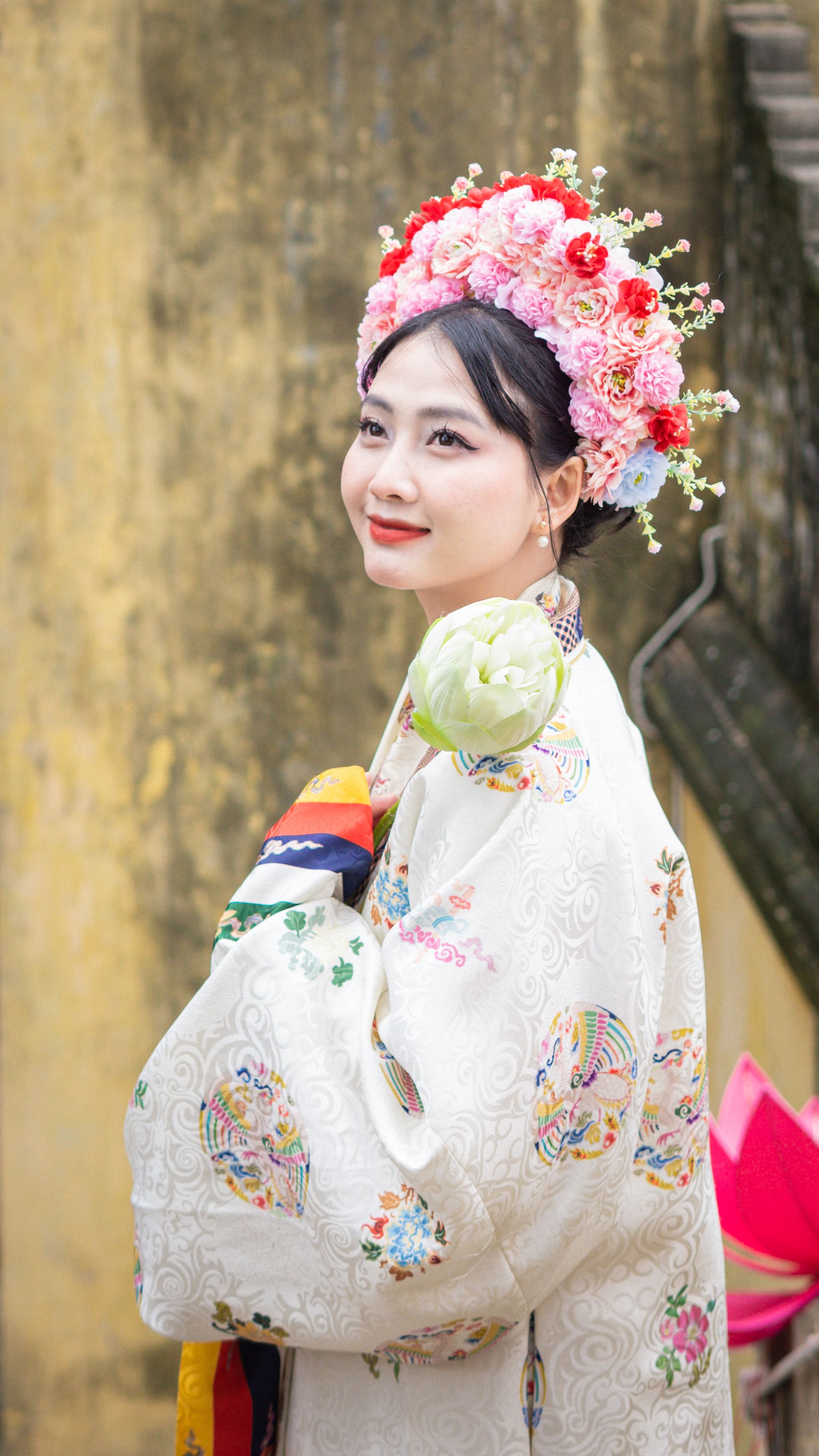 Portrait of an Asian woman in traditional attire and floral wreath, smiling in Hanoi, Vietnam.