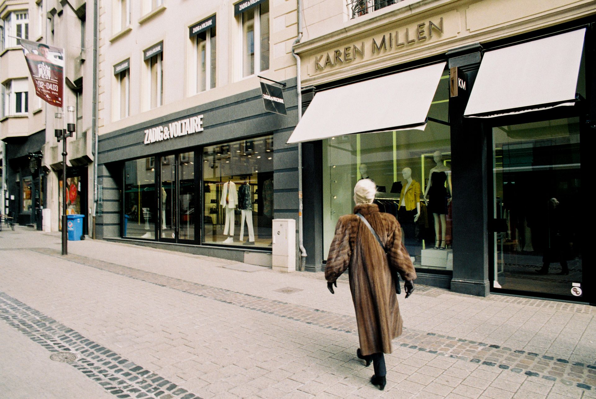 A person walks past stylish fashion boutiques on a shopping street during the day.