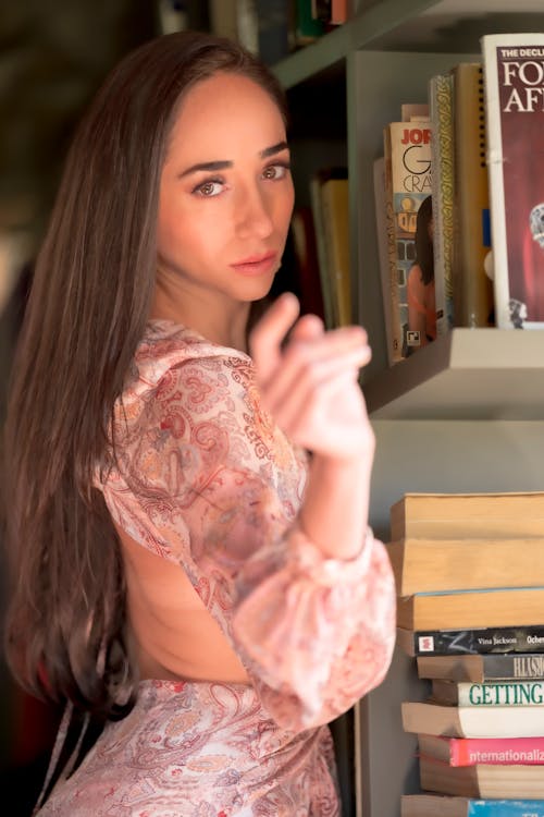 A woman in a dress pointing at a book shelf