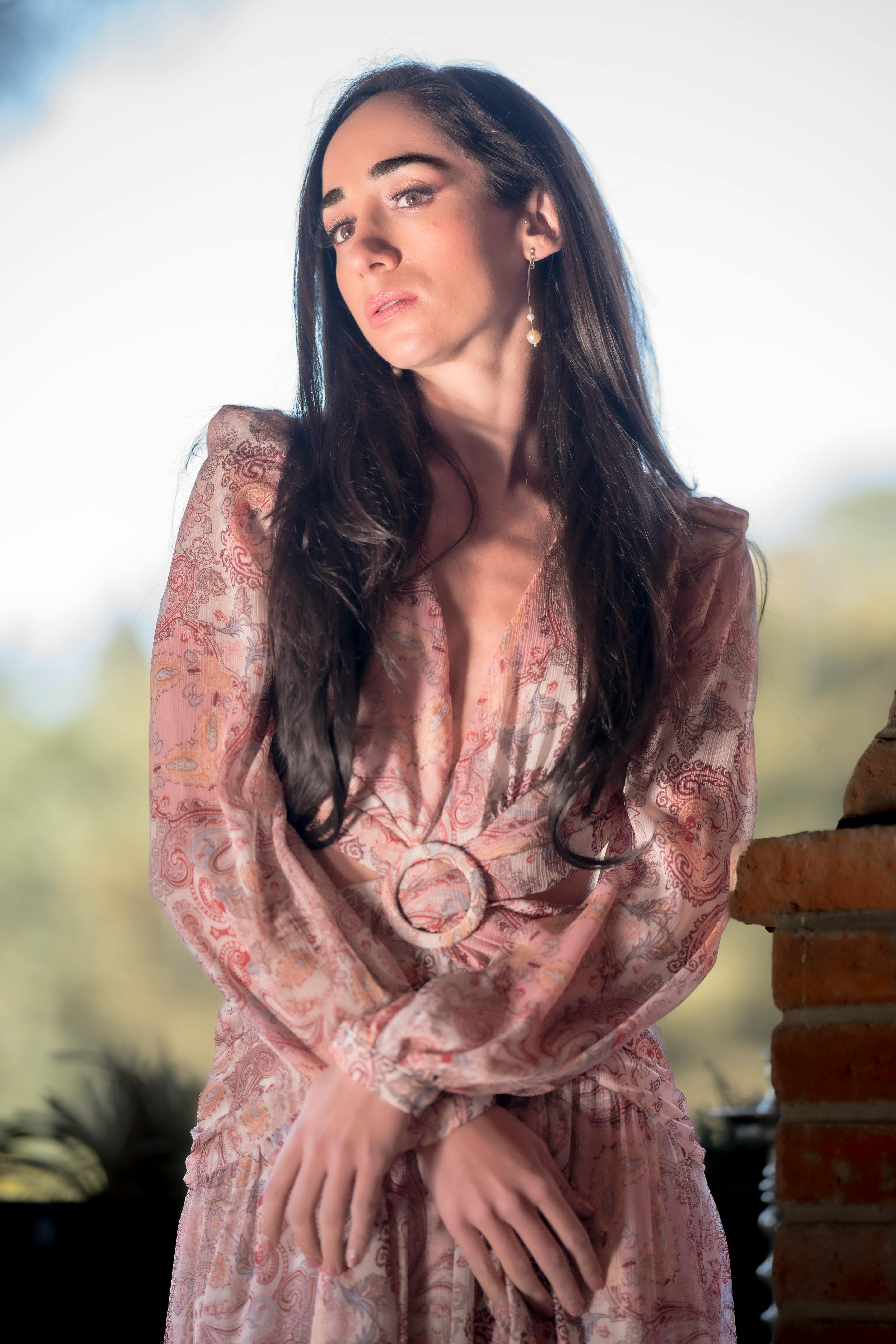 A woman in a floral dress poses elegantly against a blurred natural background.