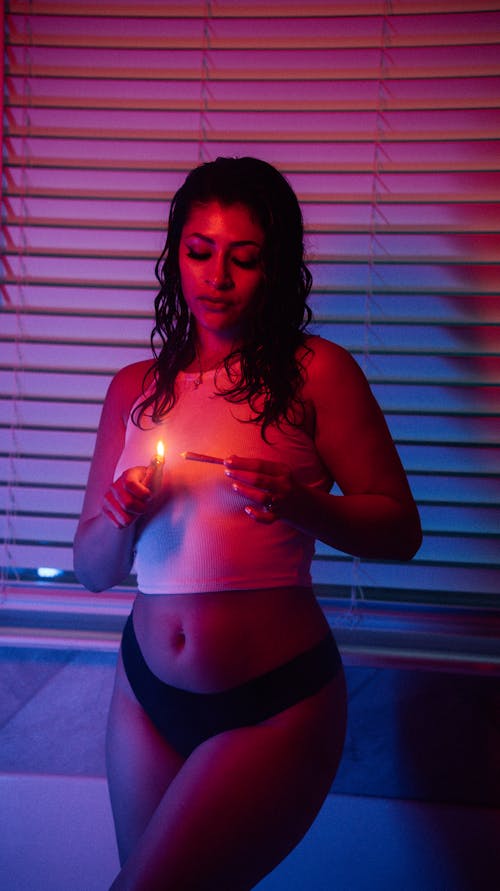 A woman in a tank top and underwear lighting a blunt 