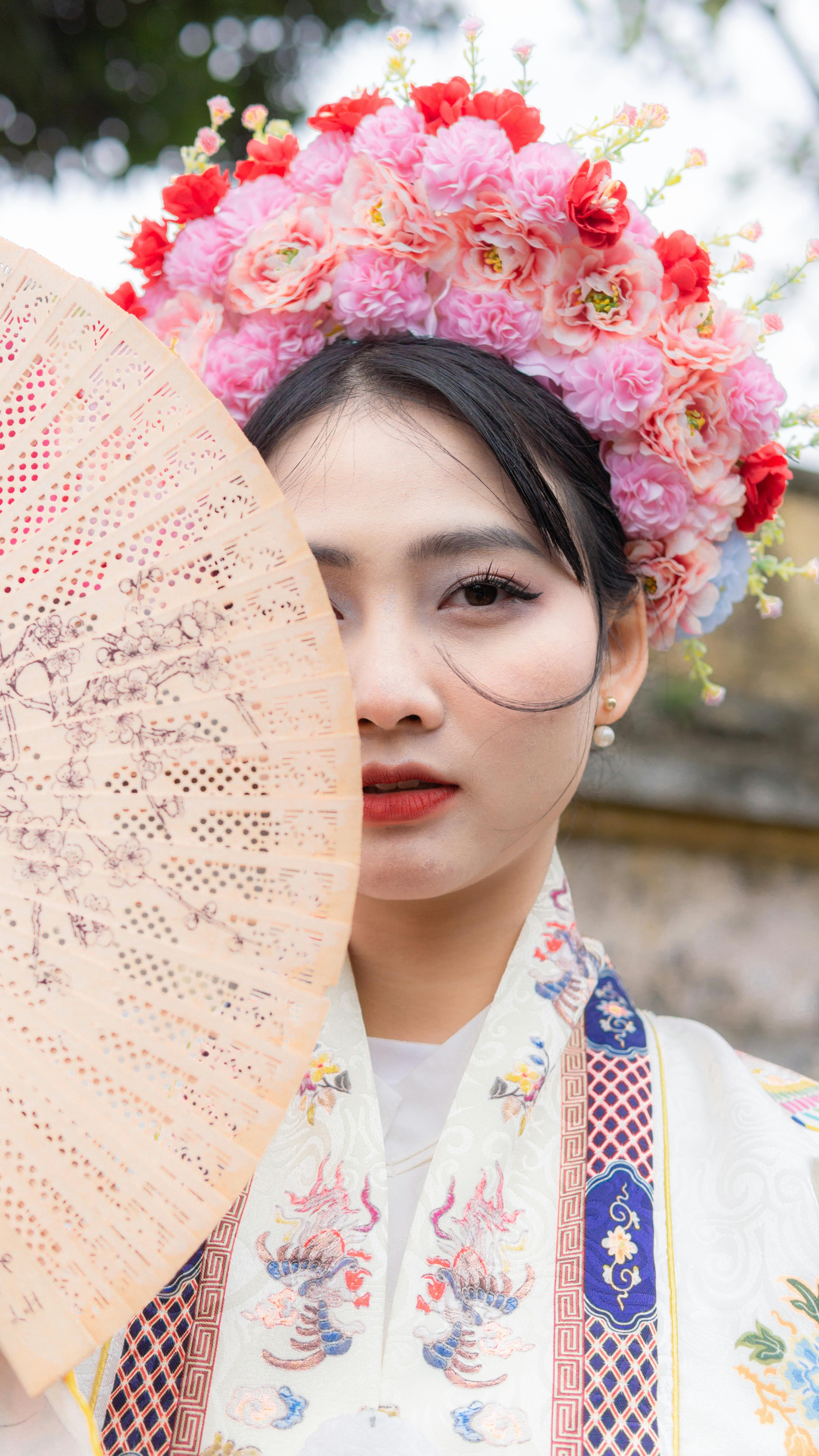 Asian woman in traditional attire with a floral headpiece holding a fan