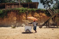 在巴西纳扎雷海滩，一名海滩小贩推着冰淇淋车走在雨伞下