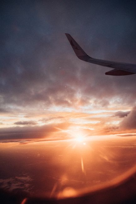 Capture the breathtaking view of a sunrise from an airplane window with golden horizon and clouds.