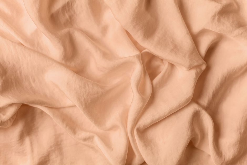 A detailed close-up shot of soft peach-colored fabric with natural wrinkles.