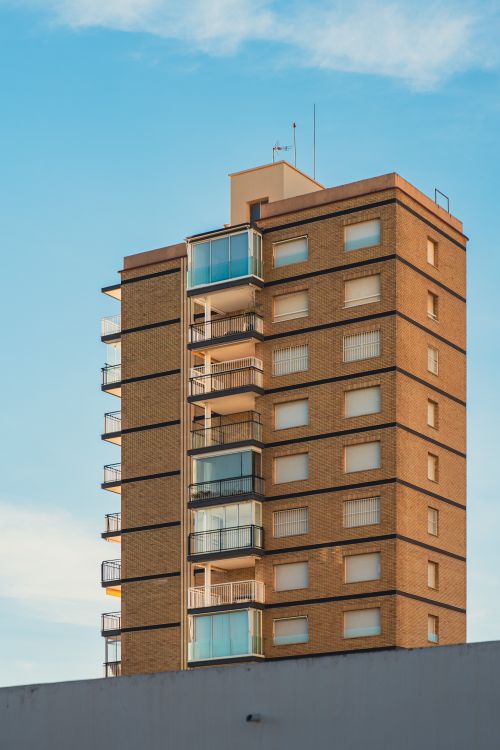 Free A modern high-rise residential building with balconies under a clear blue sky. Stock Photo
