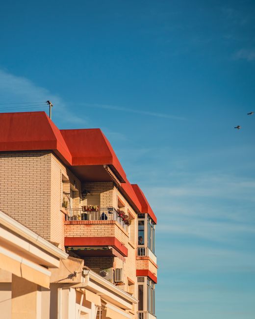 Contemporary urban architecture featuring red-roofed balconies under a clear blue sky, showcasing stylish apartments.