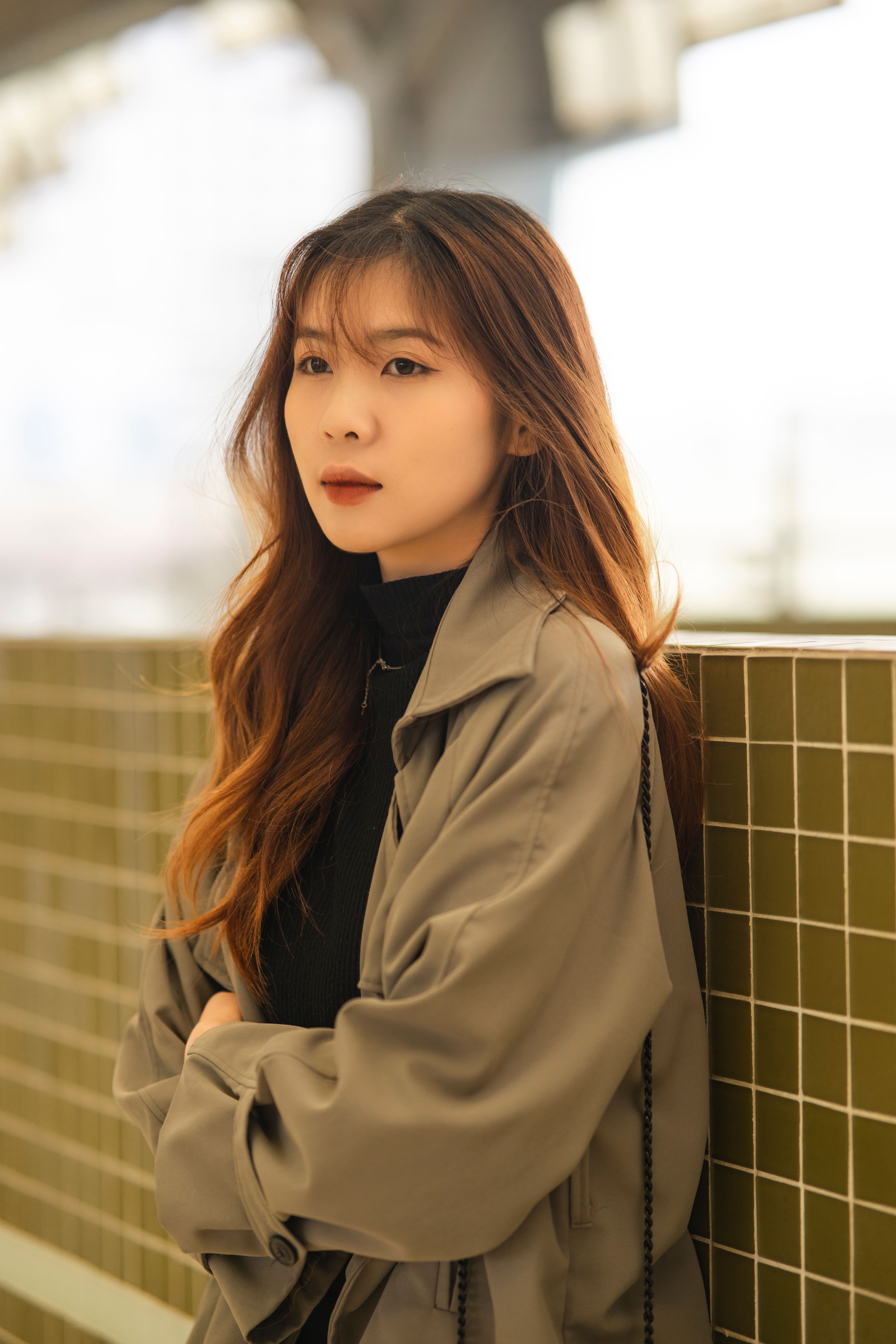 Stylish portrait of a woman with long hair in an urban environment, wearing a beige coat.