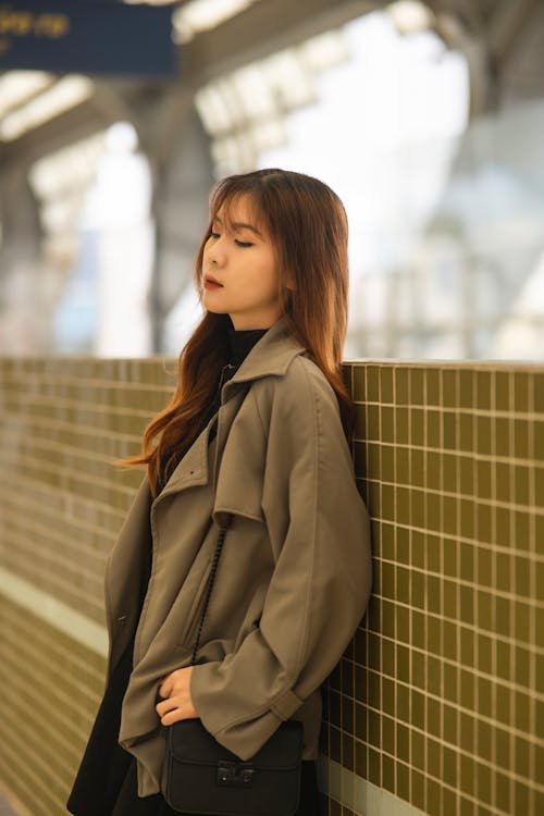 A woman in a trench coat leaning against a wall