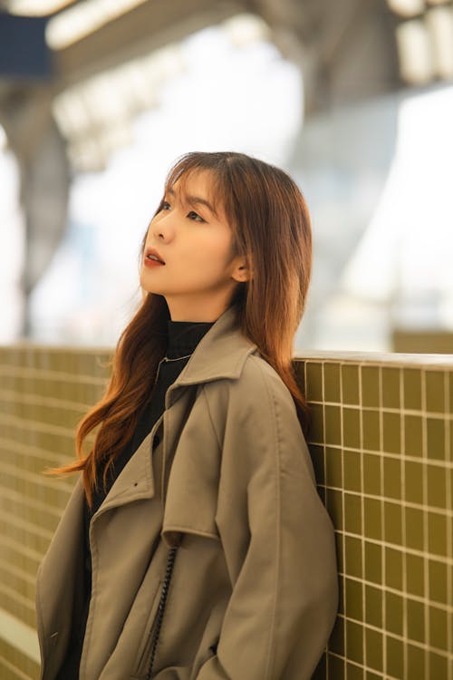 A woman in a trench coat leaning against a wall