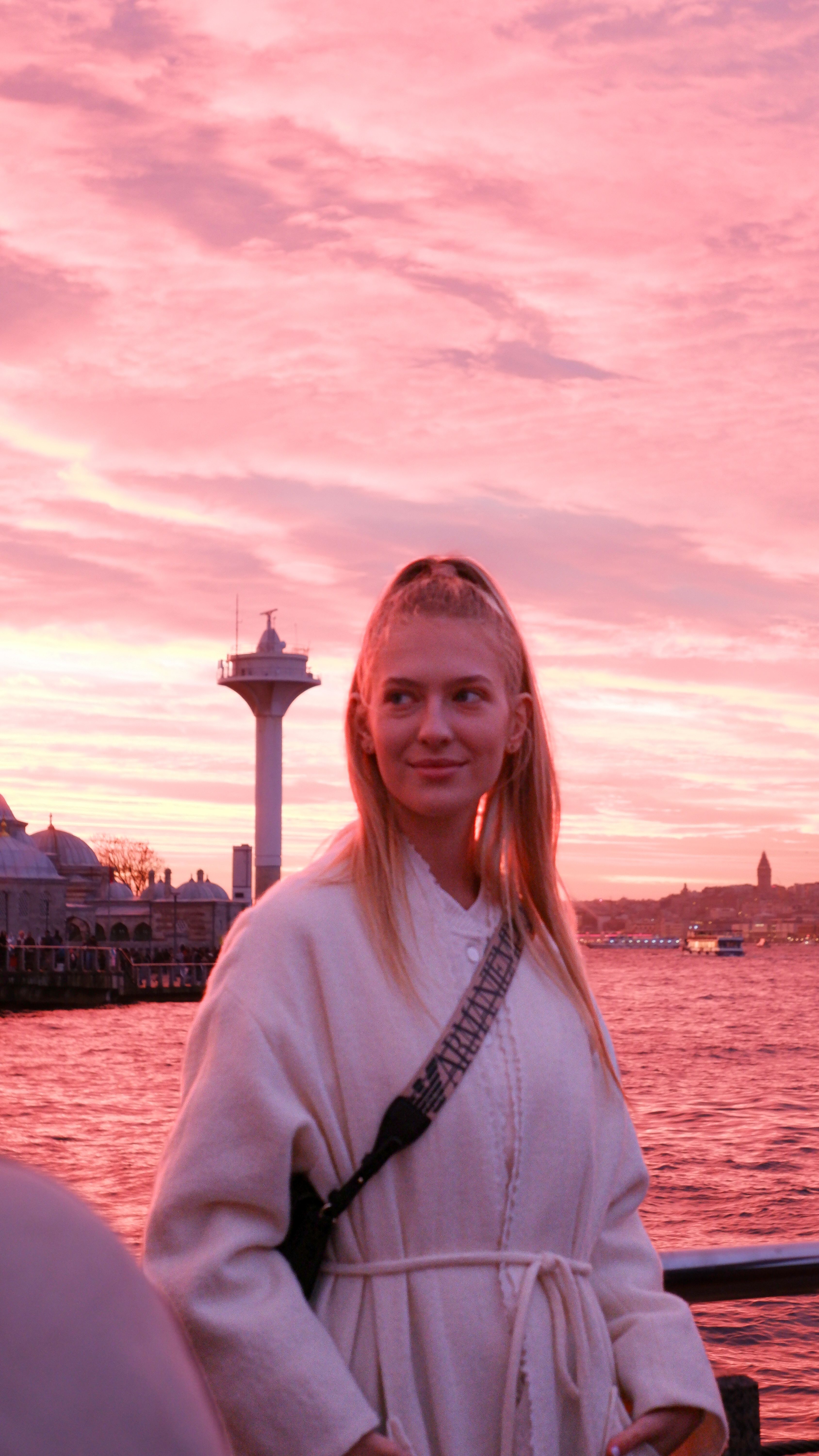 Blonde woman enjoying a vibrant sunset by the Bosporus in Istanbul, with local landmarks in the background.