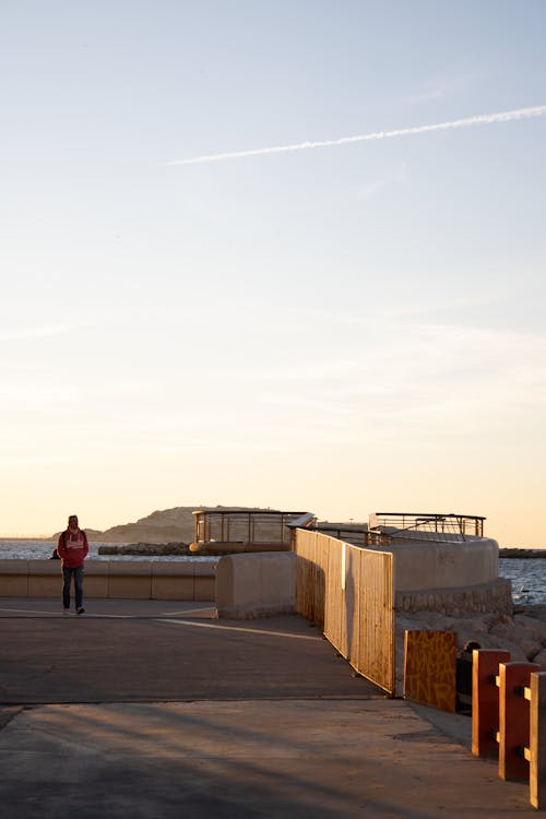 Person Walking on Promenade on Sea Shore at Sunset