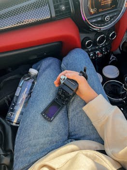Person holding a digital camera in a car interior with jeans and a sweater visible.