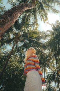 Fashionable woman in colorful clothes under palm trees enjoying a sunny day.