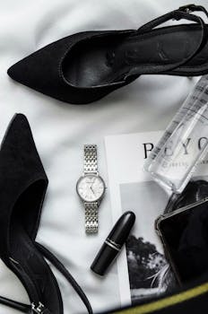 Chic display of women's fashion essentials featuring black heels, lipstick, and a wristwatch.