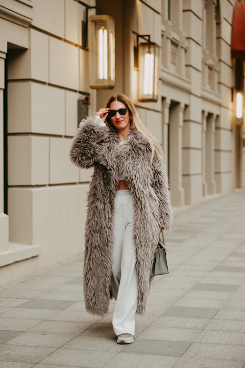 A woman in a long fur coat and white pants