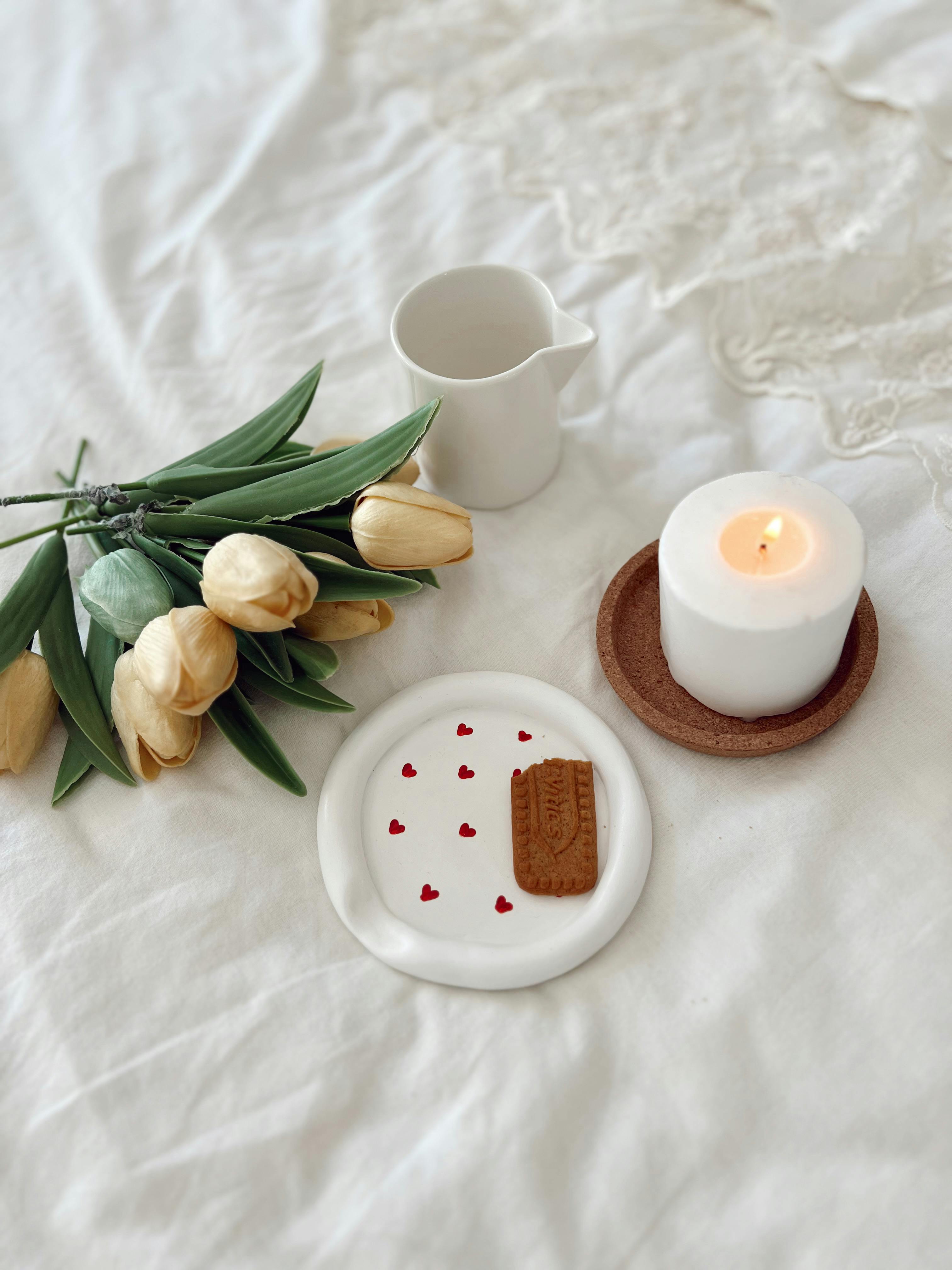 Warm and inviting composition of tulips, candle, and cookie on a white bed.