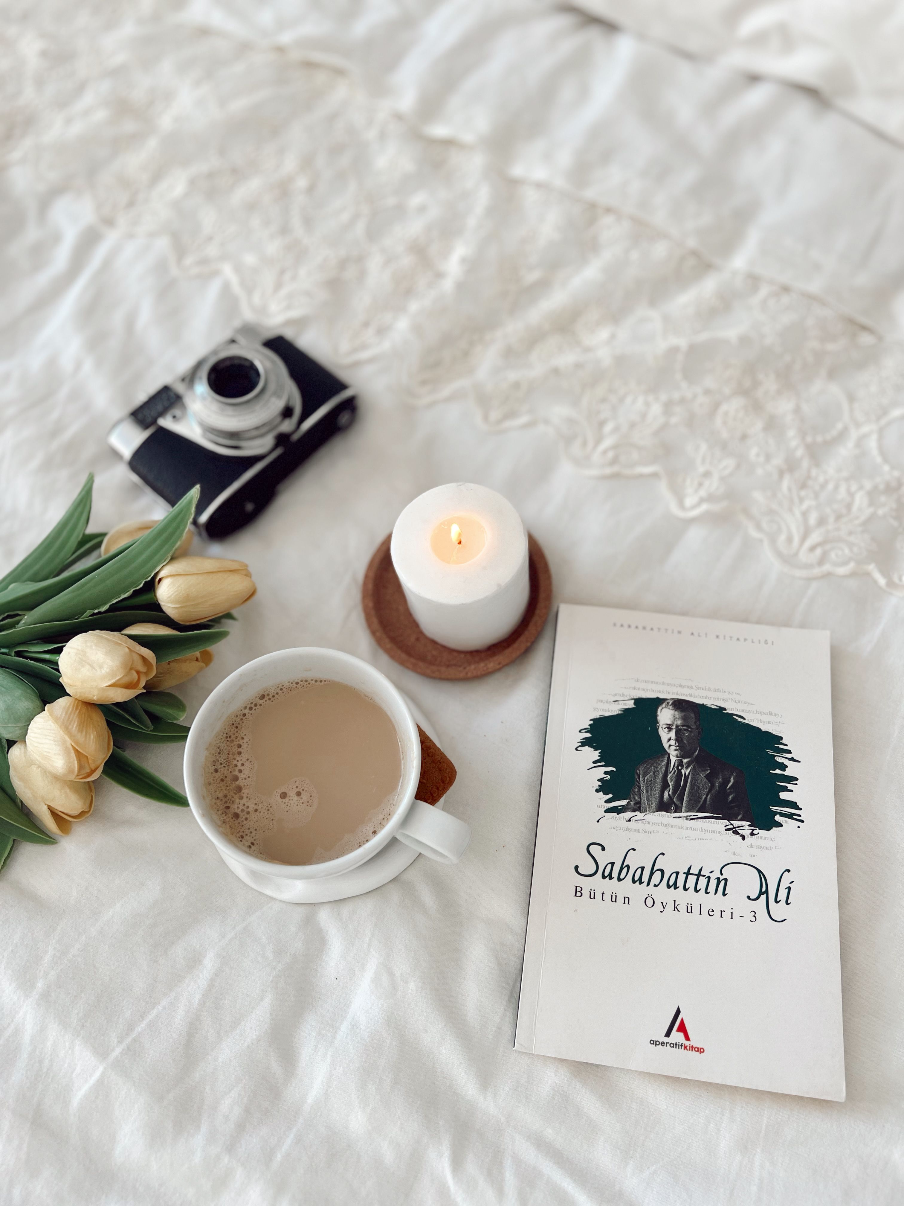 A tranquil still life featuring a book, candle, coffee, camera, and tulips on a bed.