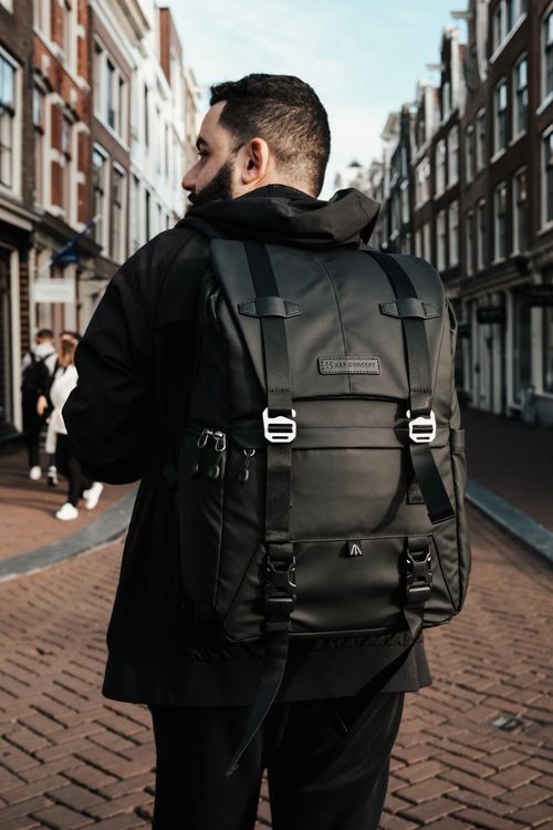 Free Man with backpack walking through urban city street. Ideal for travel and lifestyle themes. Stock Photo