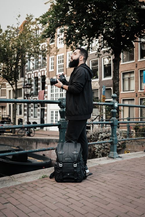 Free Man with a beard and backpack taking photos in a picturesque urban setting. Stock Photo