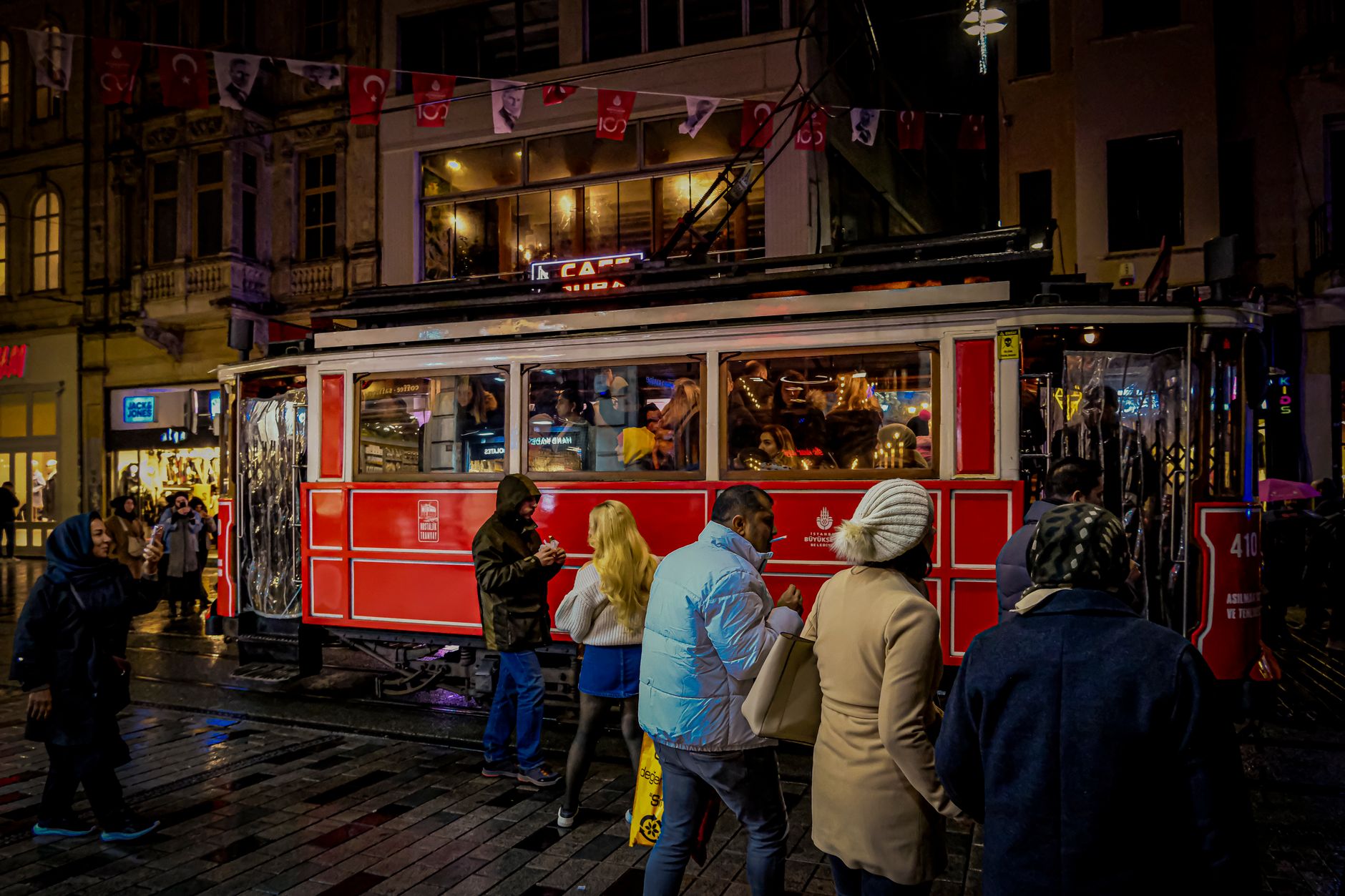 Nostalgic red tram passing through a busy street in İstanbul at night.