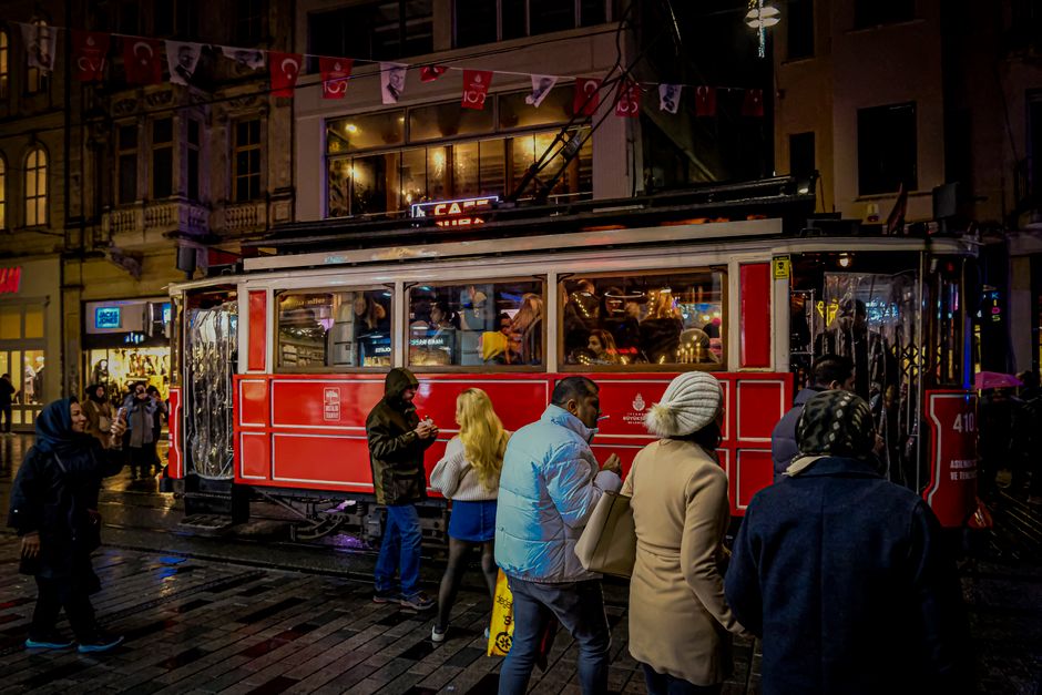 Nostalgic red tram passing through a busy street in İstanbul at night.