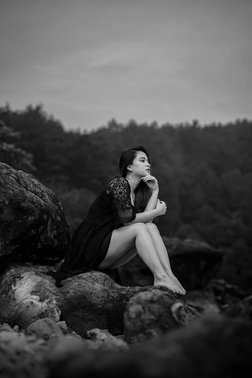 Pensive Young Woman in a Dress Sitting on the Rocks