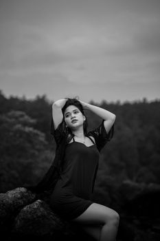 Black and white photo of a woman posing elegantly in a natural setting with hands in hair.