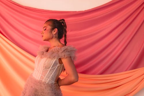 A woman in a dress standing in front of a pink and orange curtain