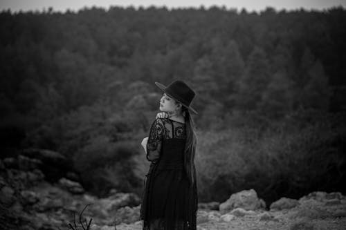 A woman in a black dress and hat standing on a rock