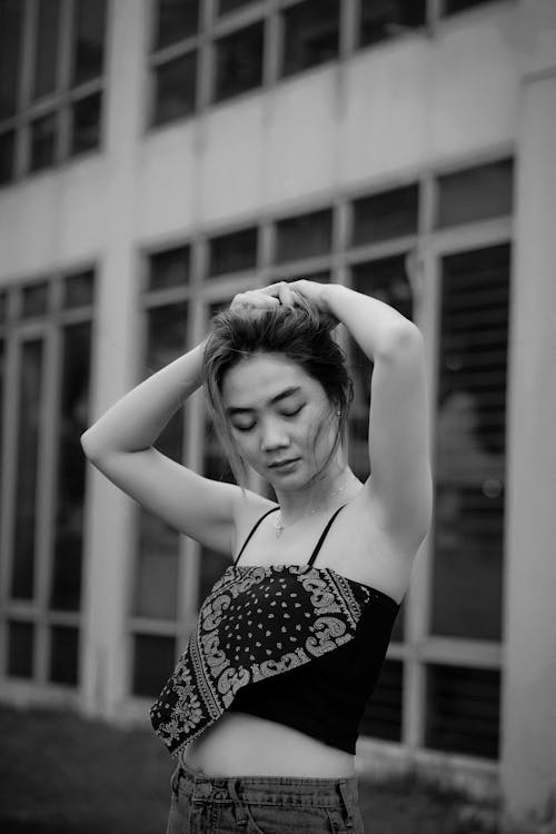 Black and White Photo of a Young Woman in a Tank Top Fixing Her Hair 