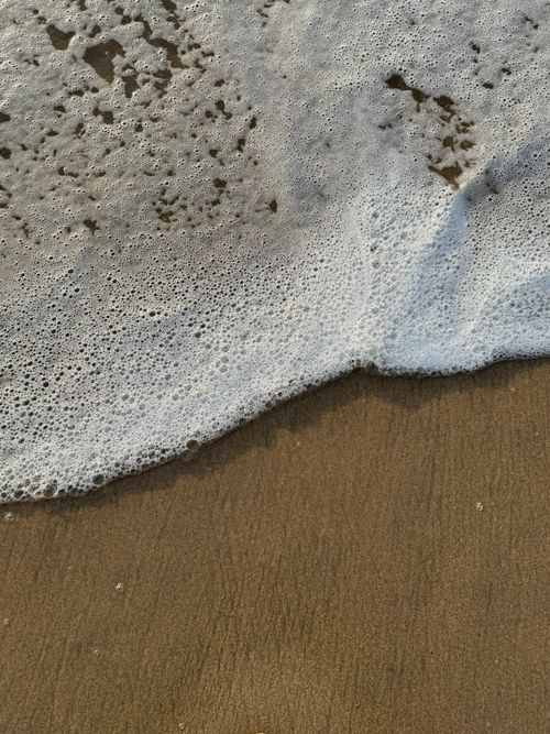 Free A close-up view of ocean waves and foam on a sandy beach top view. Stock Photo
