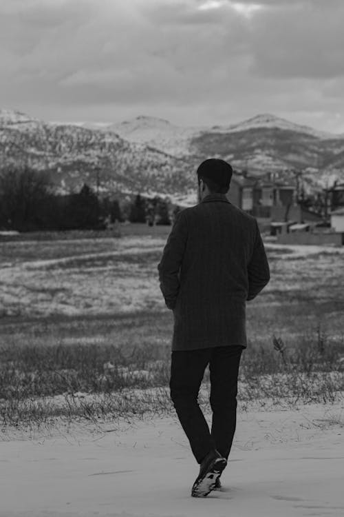 Back View of a Man Walking on a Field with Mountains in Distance 