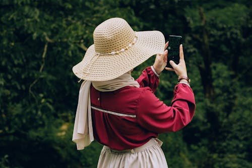 Back View of Woman in Hat and Red Shirt Taking Pictures with Smartphone