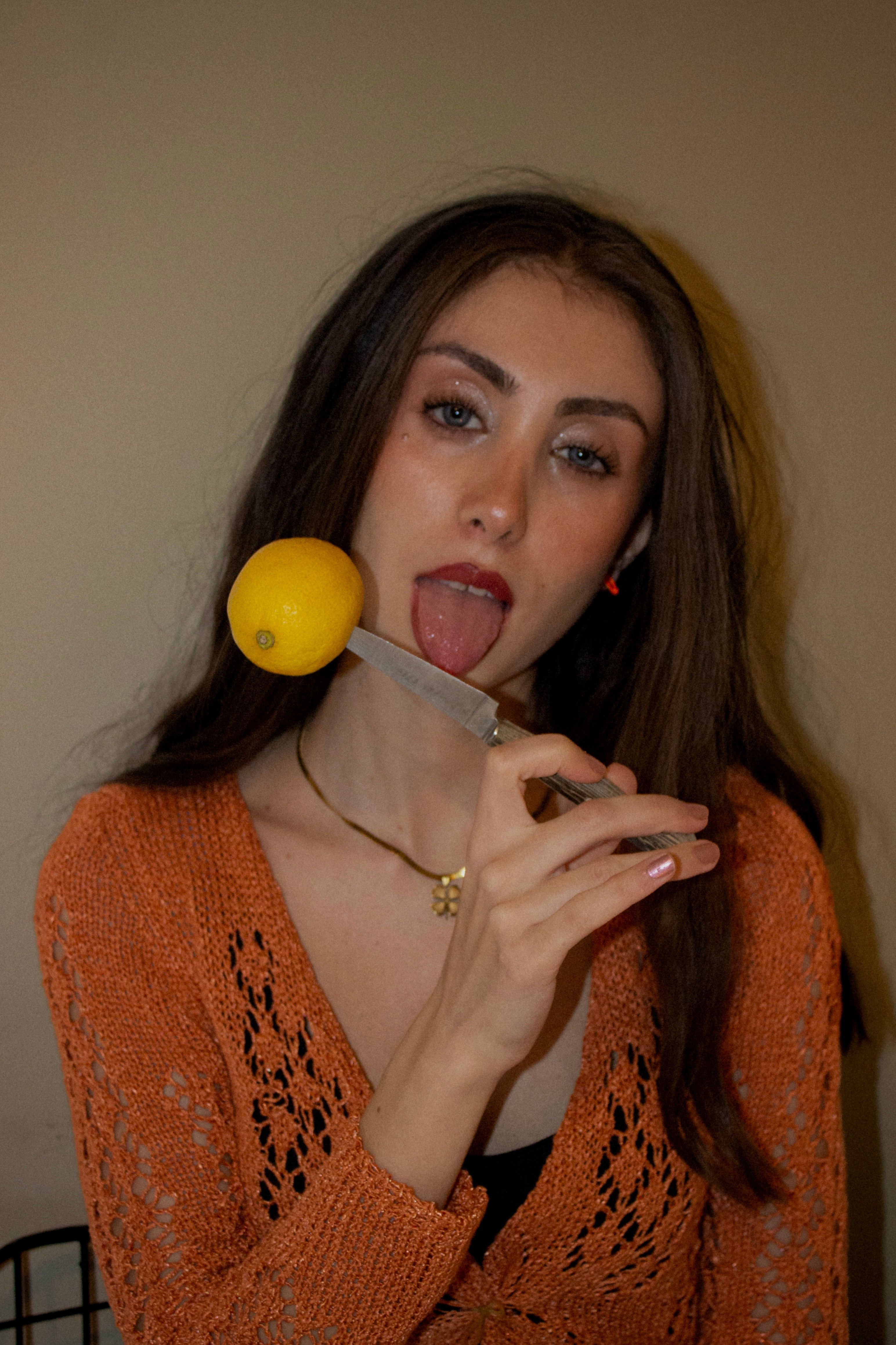 Portrait of a young woman holding a lemon on a knife, playful expression.