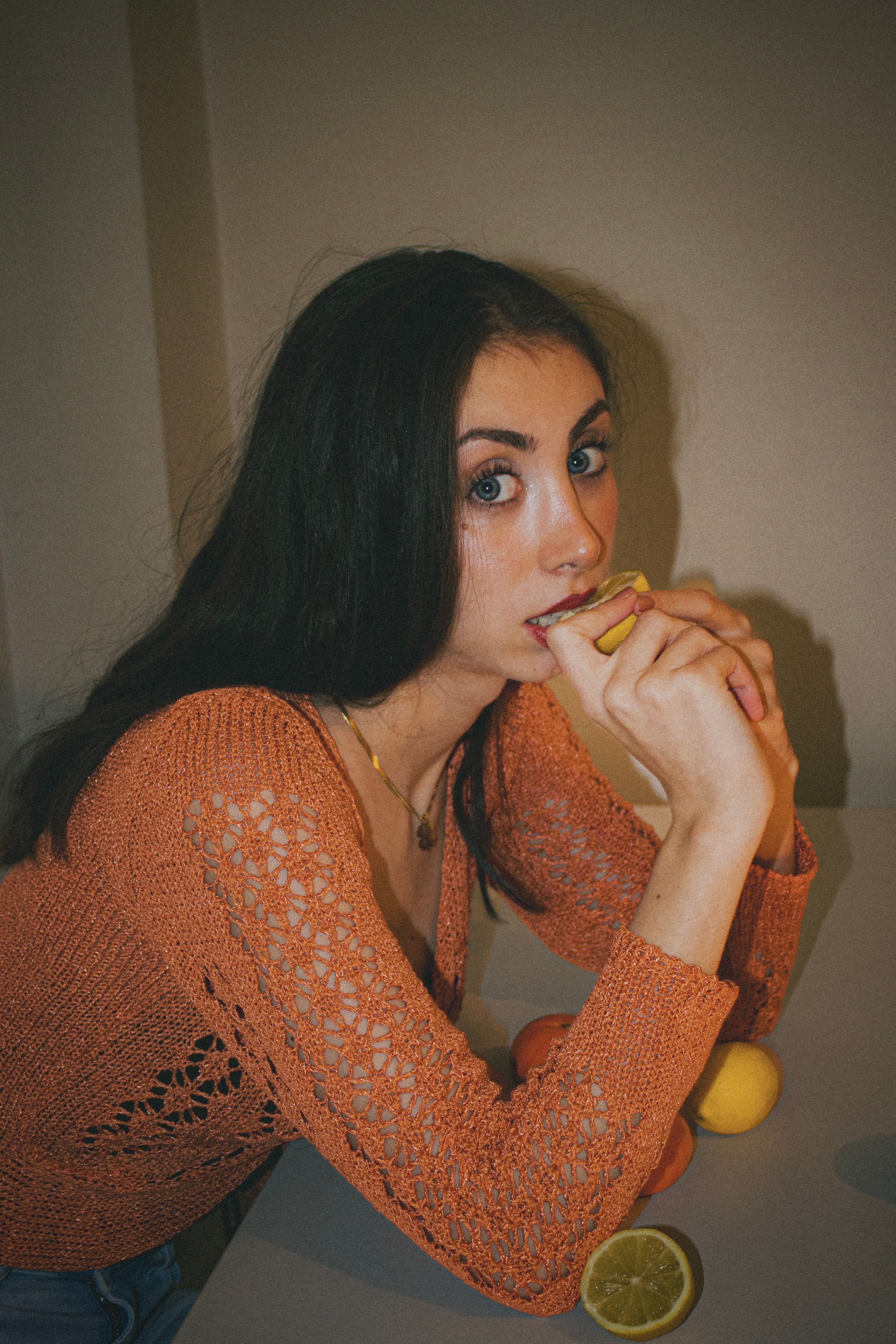 Portrait of a woman with long dark hair holding a lemon indoors in Ankara. Fashionable and vibrant setting.
