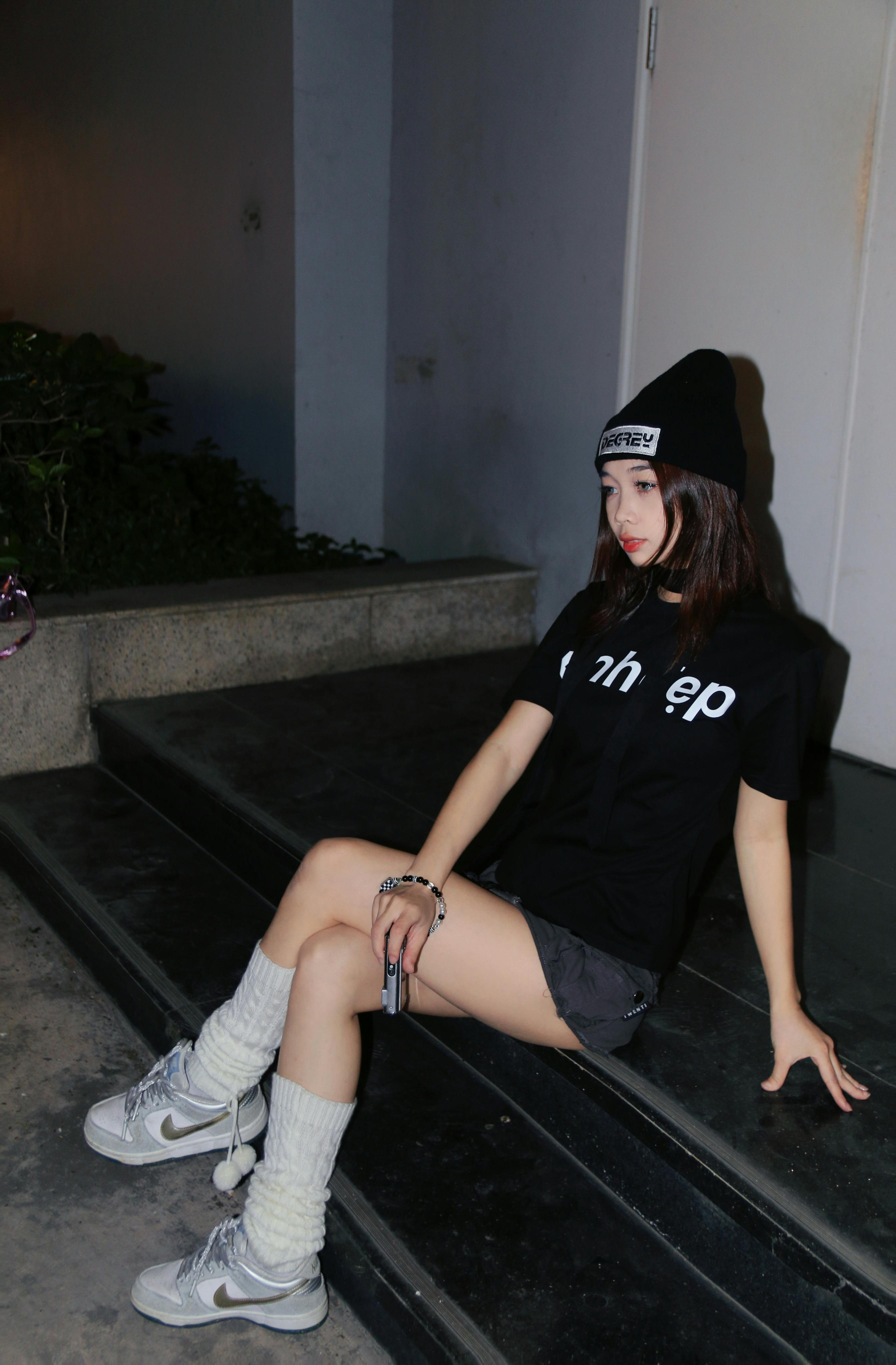 Asian woman wearing stylish black outfit sitting on stairs at night. Fashion photography.