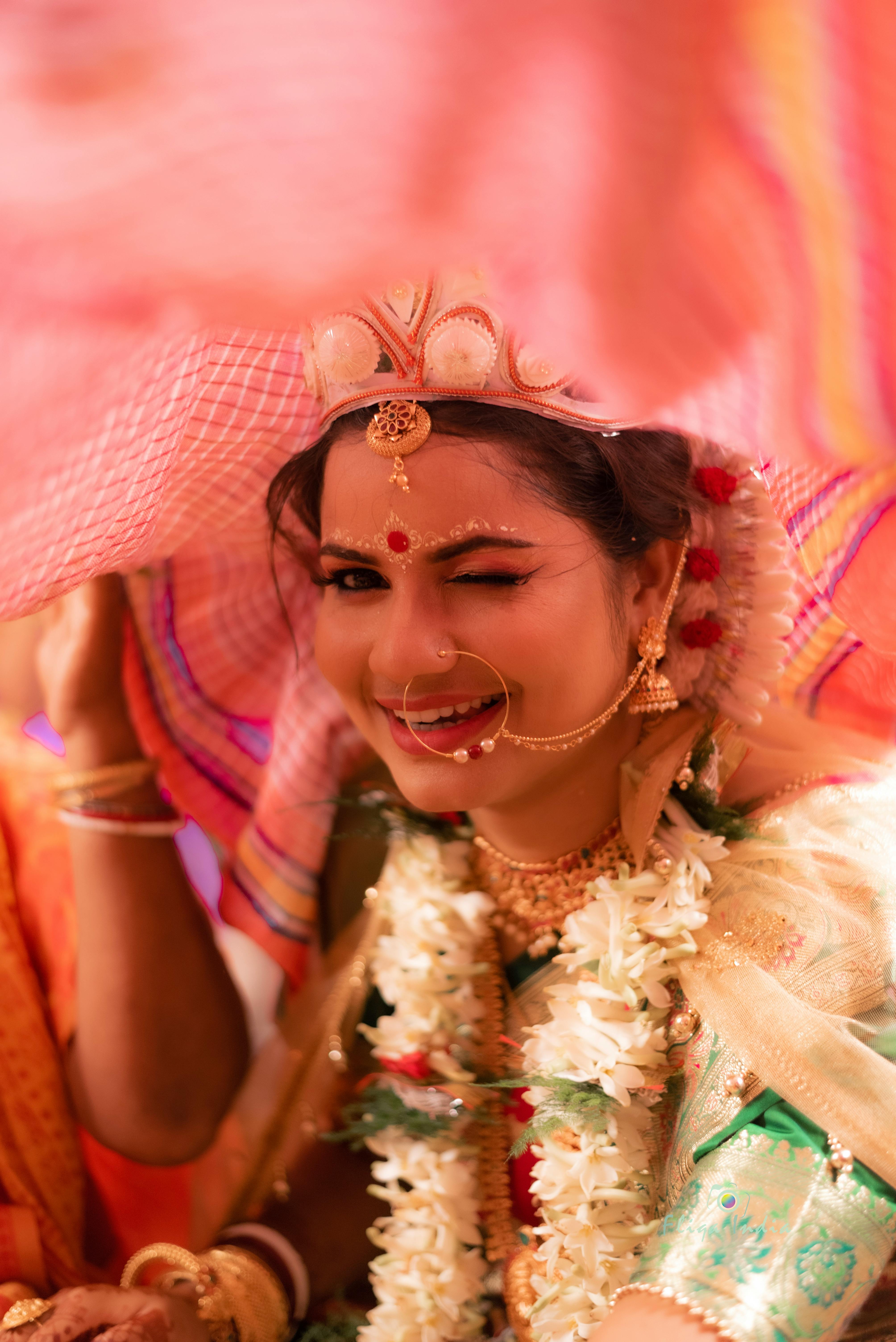 Smiling Indian bride winking in traditional attire with ornate jewelry.