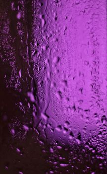 Close-up of raindrops on a glass with a vibrant purple background, creating a surreal texture.