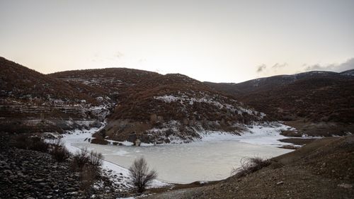 Free A serene landscape of a frozen lake surrounded by snow-dusted hills during winter dusk. Stock Photo