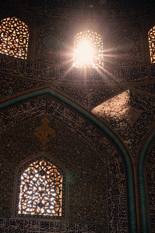 Free Sunlight streaming through ornate mosque windows highlights intricate Arabic calligraphy and patterns. Stock Photo