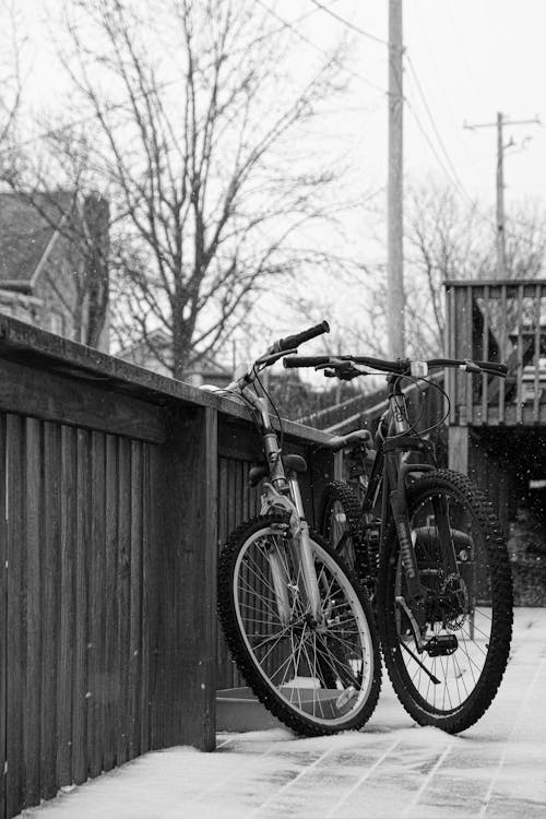 A black and white photo of two bicycles leaning against a fence