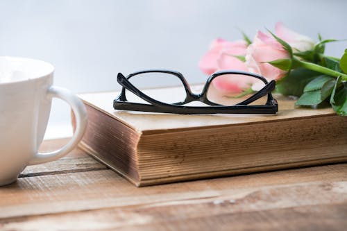 Kostenlos Brillen Auf Buch Neben Pink Rose Auf Tasse Stock-Foto