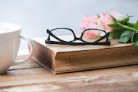 木桌上摆放着咖啡杯、玻璃杯、书和粉红玫瑰，构成了一幅宁静的场景