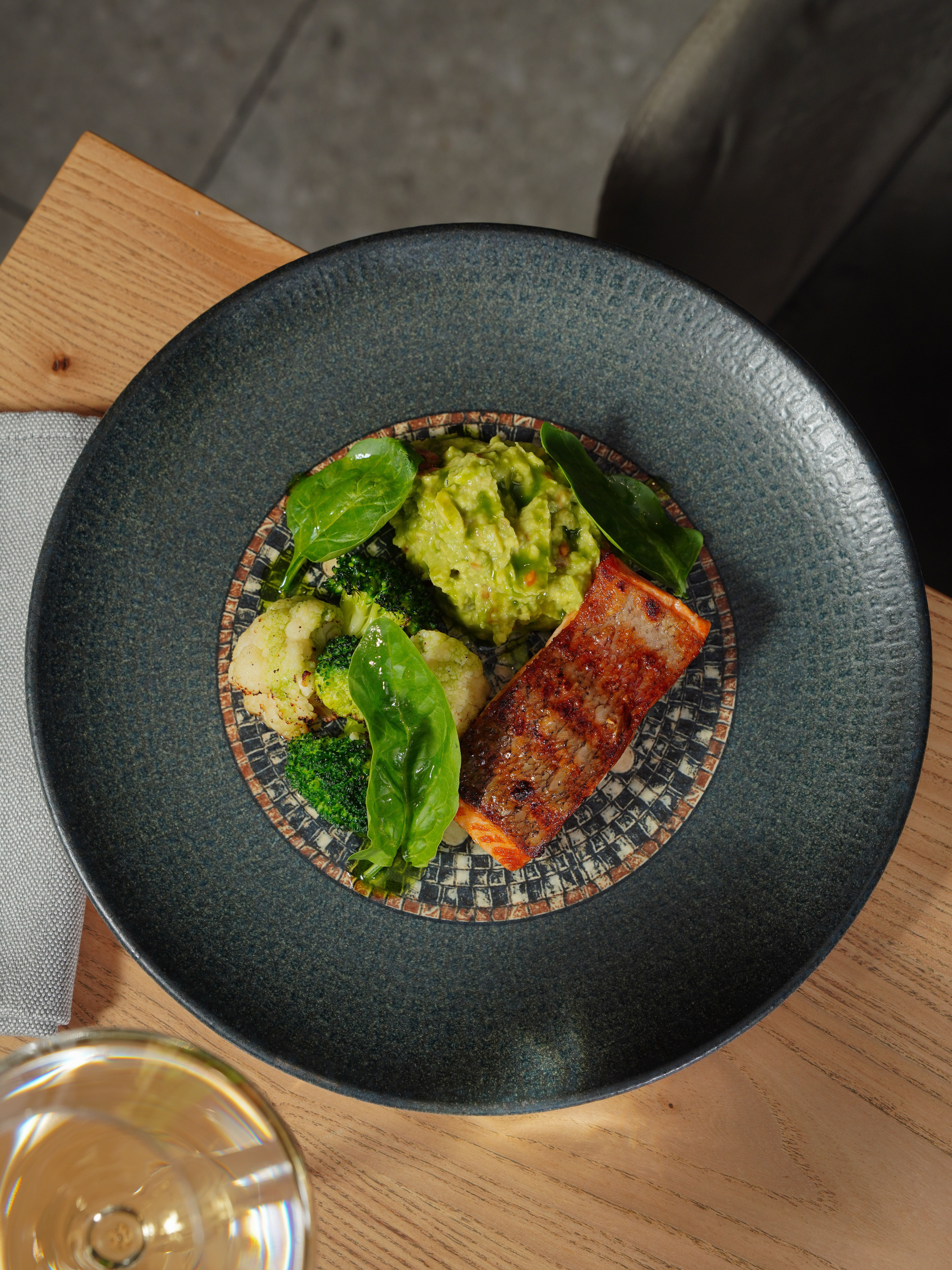 Exquisite salmon served with guacamole and greens on a designer plate, showcasing food artistry.