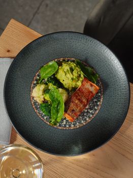 Exquisite salmon served with guacamole and greens on a designer plate, showcasing food artistry.