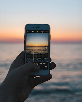 A close-up of a hand holding a smartphone photographing a serene sunset over the sea in Zonguldak, Türkiye.