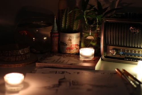 Free A warm still life of a cozy desk setup featuring candles, a vintage radio, and indoor plants. Stock Photo