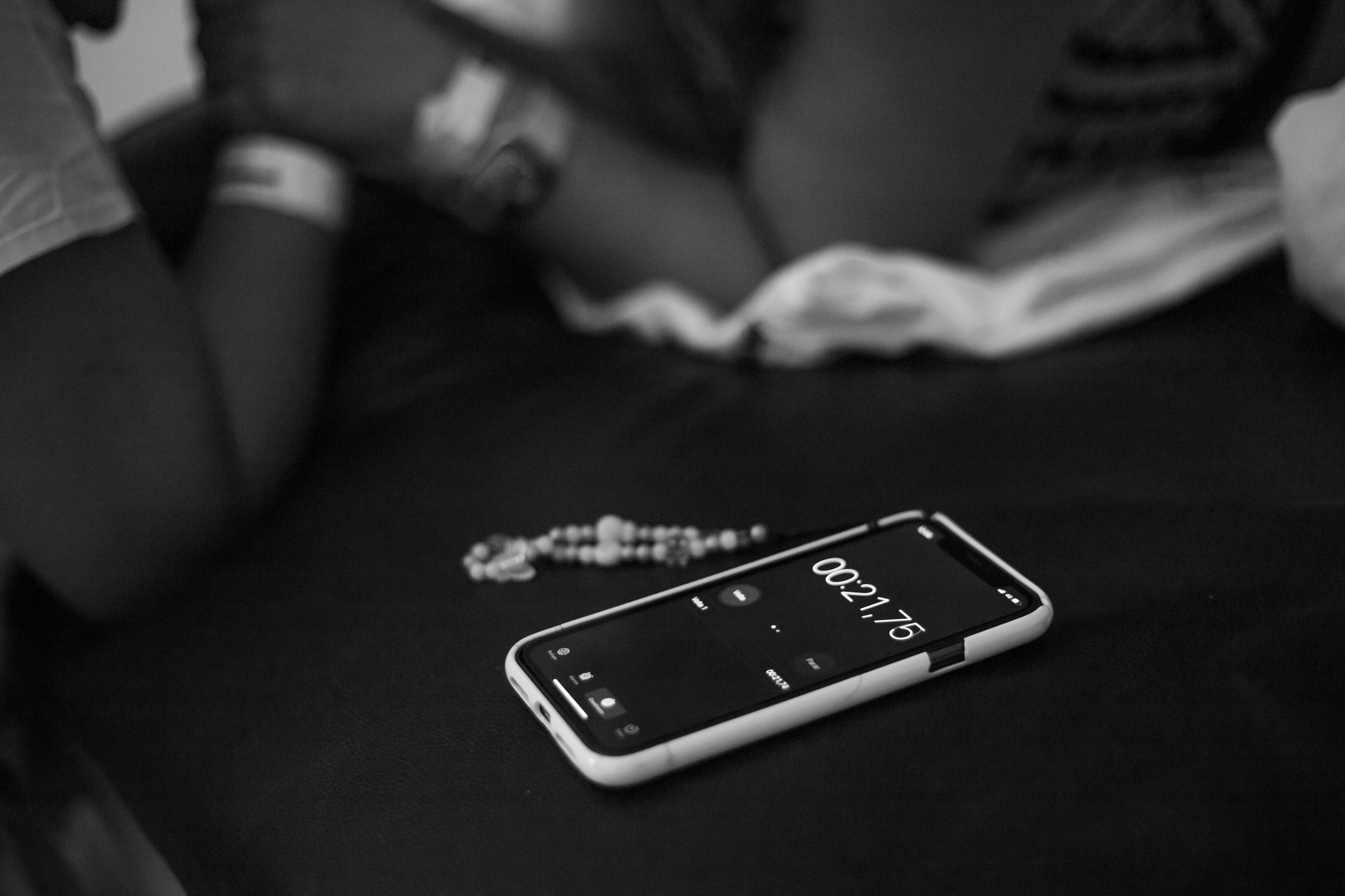 Black and white image of a smartphone timer alongside a bracelet and blurred hands.