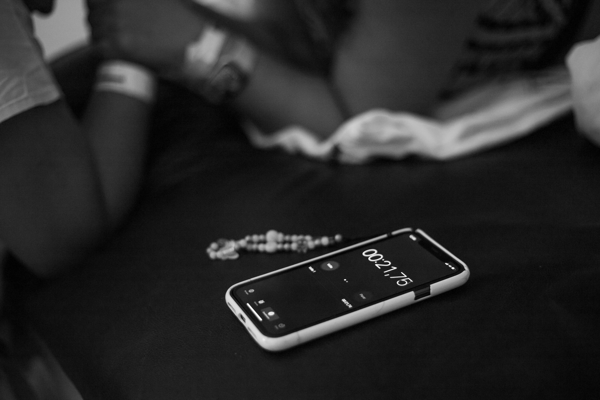 Black and white image of a smartphone timer alongside a bracelet and blurred hands.